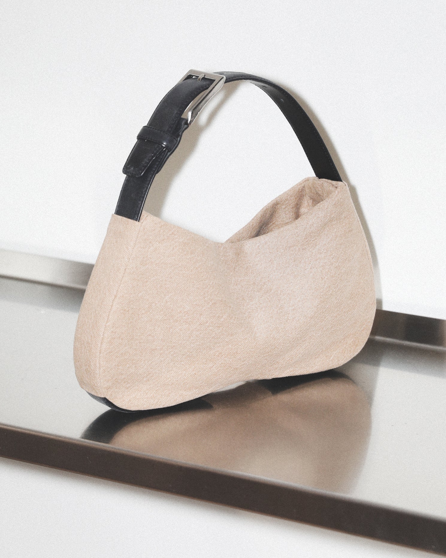 Beige handbag with black strap on a reflective surface