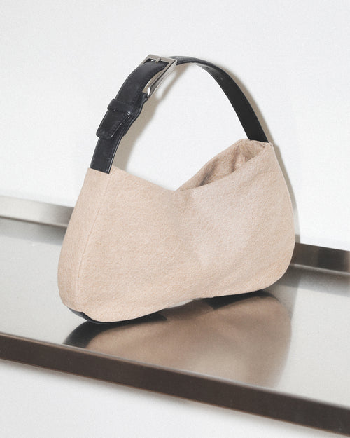 Beige handbag with black strap on a reflective surface