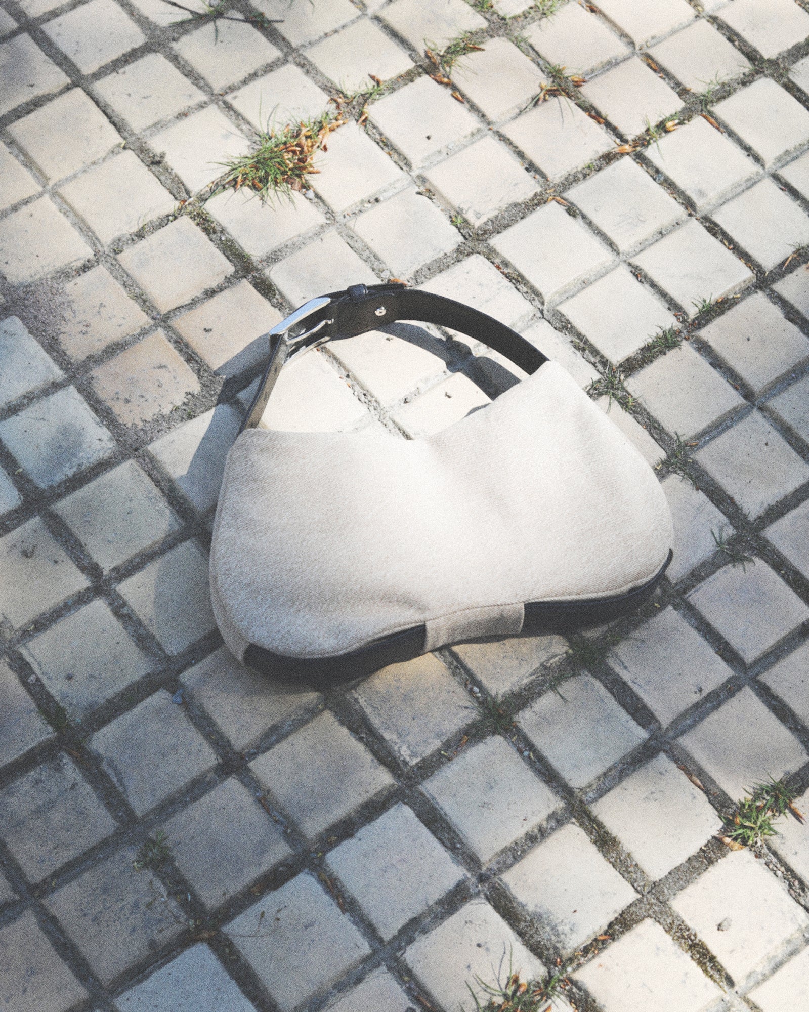 Beige shoulder bag with black strap on a textured pavement
