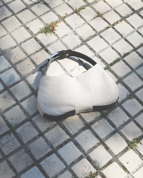 Beige shoulder bag with black strap on a textured pavement