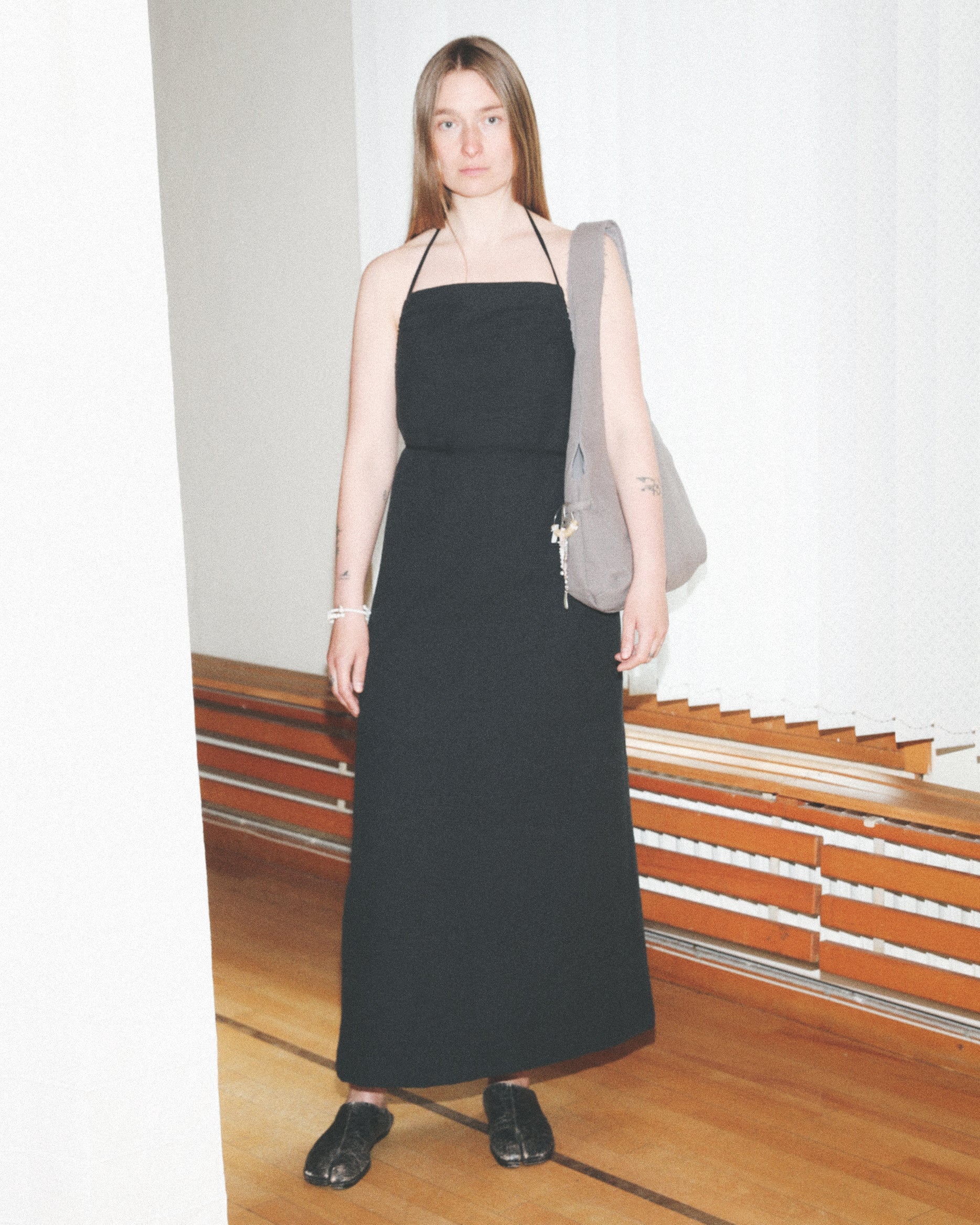 Woman wearing a black dress holding a gray bag indoors.